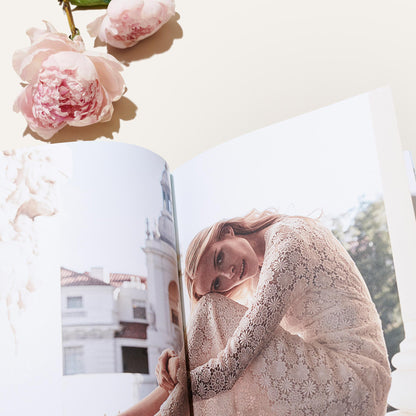 An open magazine with a photo of a woman in lace sits beside pink peonies, evoking the elegance of Margaux’s Bridal Swatch Kit on a light surface.