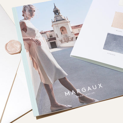 A bridal fashion magazine titled Margaux features a model in a white dress on the cover, alongside an envelope and a color sample card from the Bridal Swatch Kit by Margaux’s bespoke bridal collection.