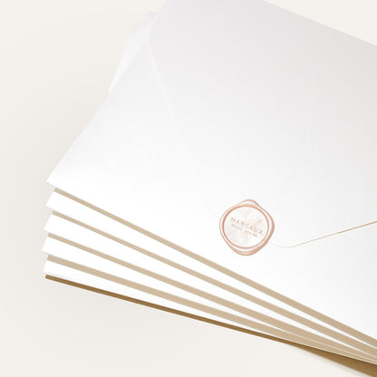A stack of white envelopes, each sealed with a pale pink wax seal stamped “MARGAUX” in gold, displays the Margaux Bridal Swatch Kit—an elegant introduction to the brand’s bespoke bridal collection. The envelopes are fanned out on a neutral background.