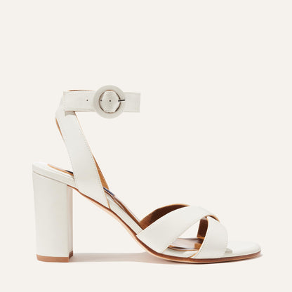 The Uptown Sandal - Ivory Nappa by margaux-development features a thick block heel, crisscross toe straps, and a round-buckle ankle strap—ideal as a formal sandal. Shown against a plain light background.