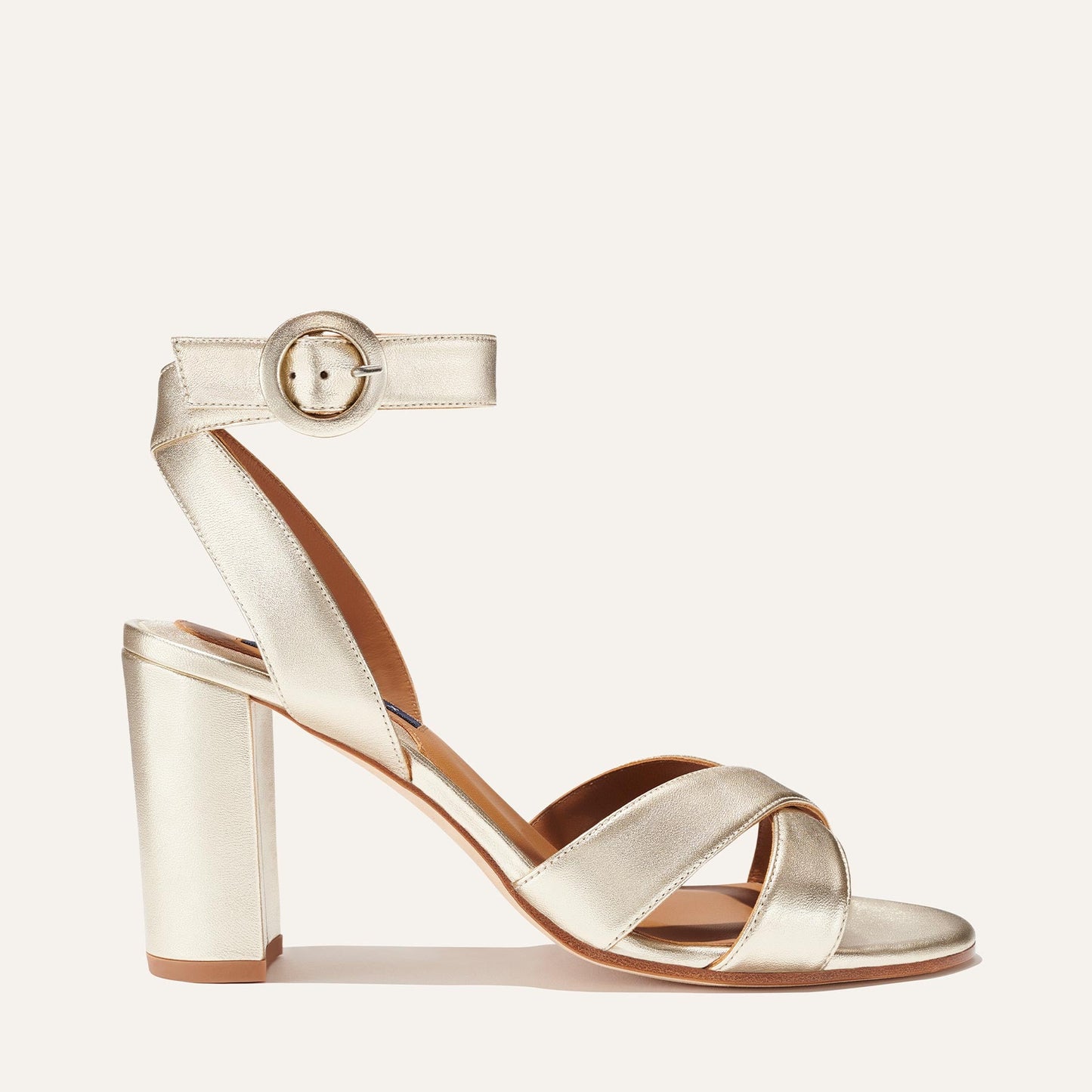 The Uptown Sandal - Champagne by margaux-development is showcased on a light background, featuring metallic crisscross toe straps, a thick ankle strap with round buckle, and a comfortable chunky block heel.