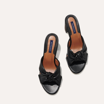 The Carmine Mule in Black Nappa, a slide-on heel featuring a plush knot detail and comfortable 2.5-inch block heel
