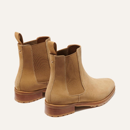 The Chelsea Boot - Sand Suede by Margaux features tan suede, elastic side panels, pull tabs at the back, and wooden soles, displayed on a light background.