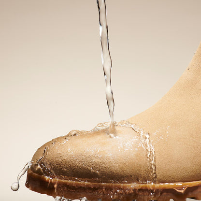Water streams onto the toe of Margaux's The Chelsea Boot - Sand Suede, causing droplets to bead and roll off, showcasing the boot’s water-resistant properties.