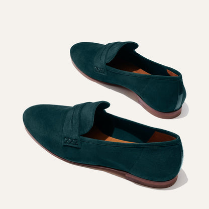 The Penny - Emerald Suede loafers by Margaux feature dark green Italian suede, brown soles, and a classic strap detail. Displayed on a light background, they offer a glove-like fit for effortless comfort.