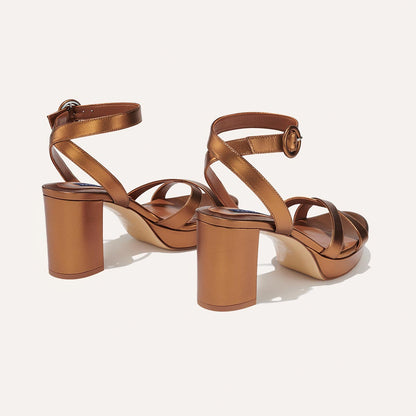 The Platform Sandal - Bronze Nappa by margaux-development features metallic bronze crisscross straps, thick comfortable platform heels, and ankle straps with round buckle closures, all displayed on a light background for an elevated look.