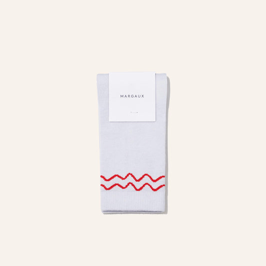A pair of The Crew Sock - Sky by Margaux in light gray with a wavy red line near the cuff, neatly folded with a Margaux label on top, displayed against a plain light background.