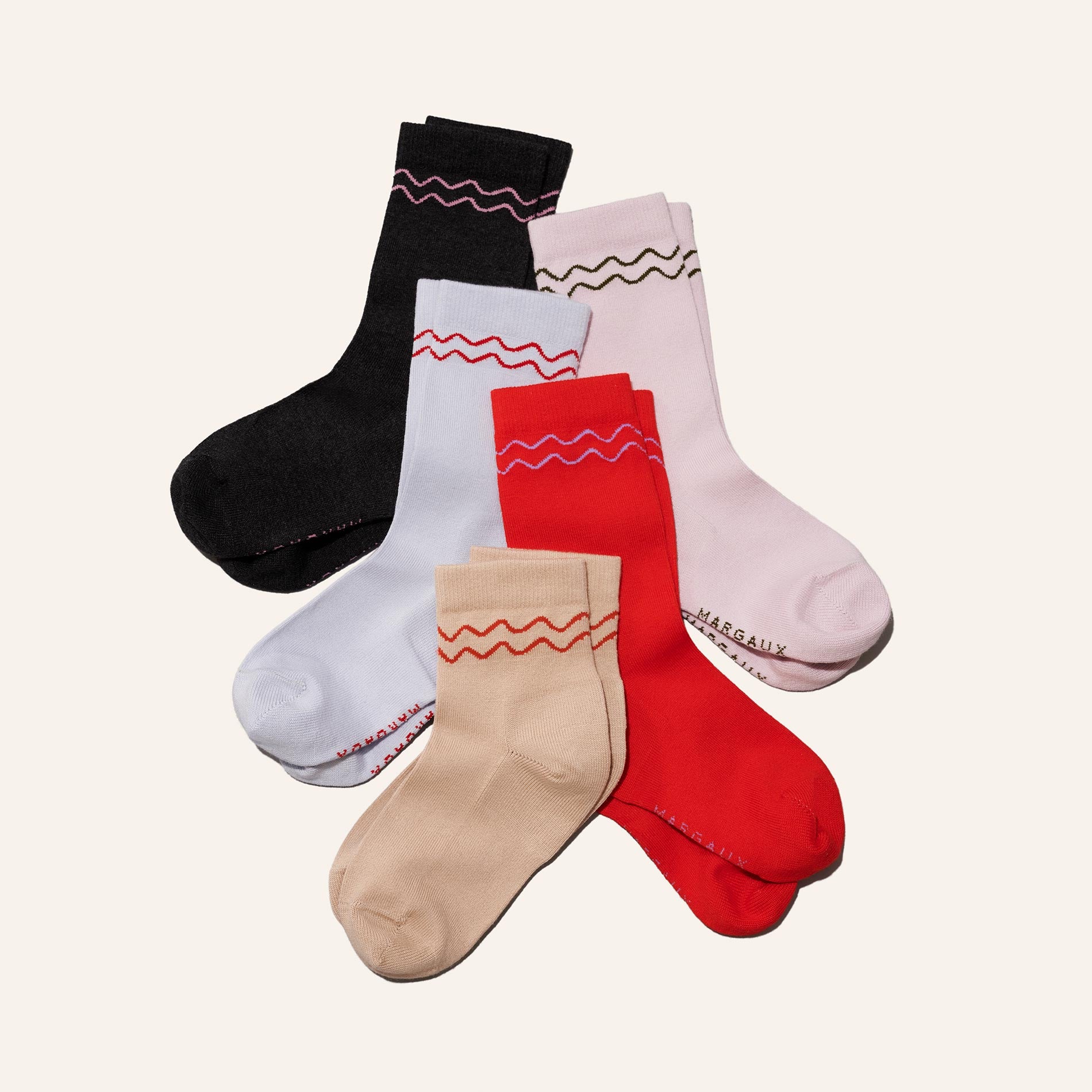Five pairs of Margaux's The Boot Sock in Camel, each featuring a wavy trim at the top, are arranged overlapping on a plain light background.