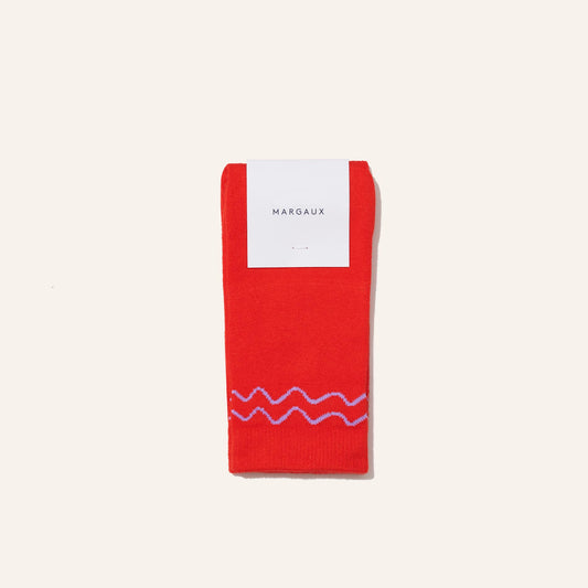 A pair of Margaux's The Crew Sock - Poppy in bright red with a pink wavy line near the ankles, folded neatly with a white Margaux label on top, set against an off-white background. Ideal for gift box sets.