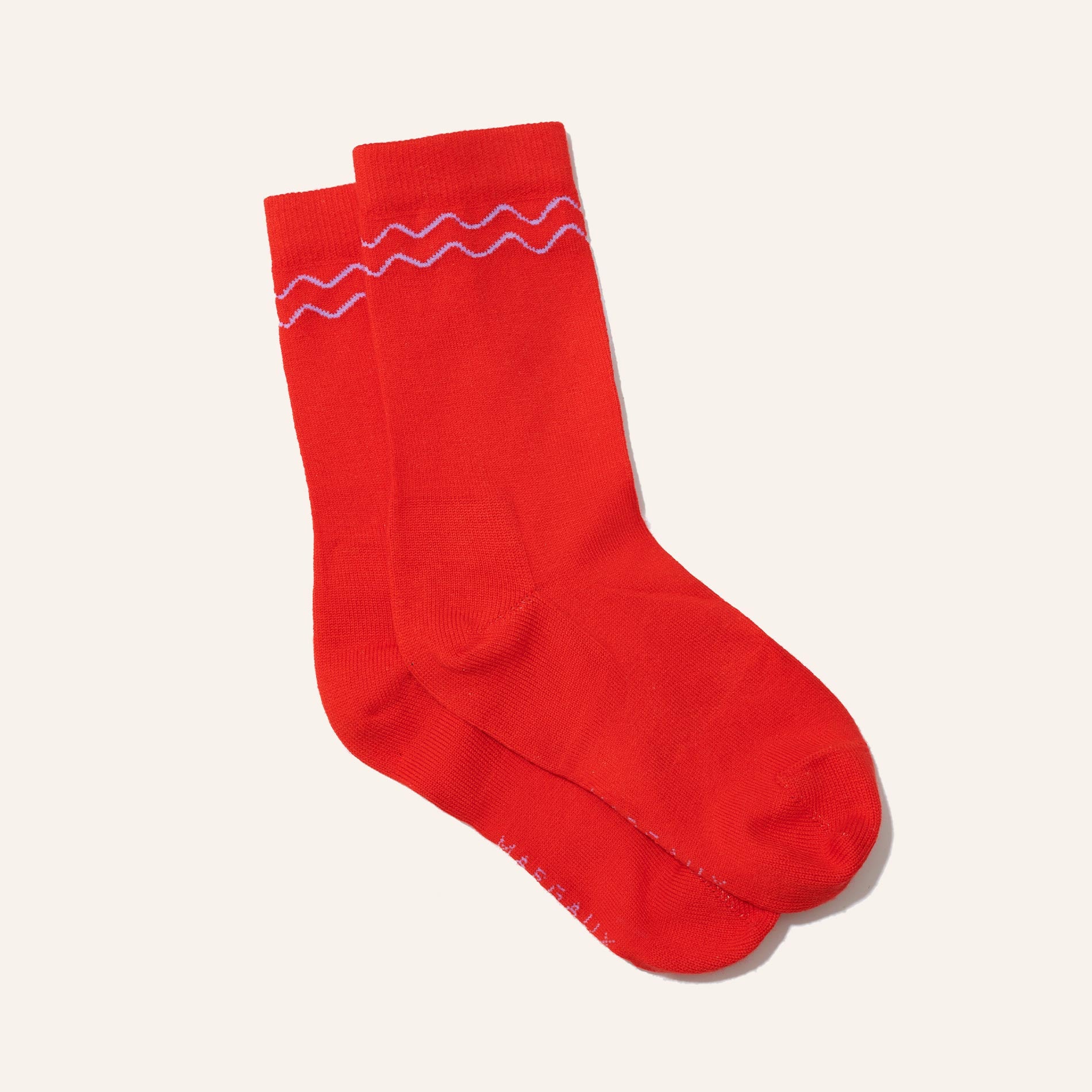 The Crew Sock - Poppy by Margaux: a pair of bright red cozy socks with a simple white wavy line near the top, shown on a plain light background.