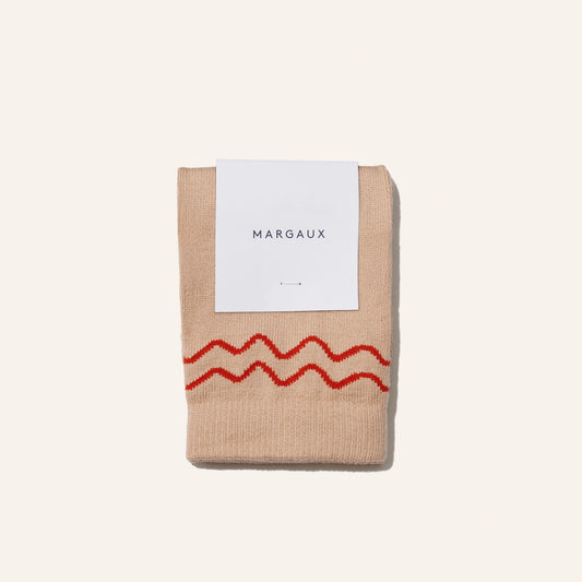 The Boot Sock - Camel by Margaux: cozy beige socks with two wavy red stripes near the top, neatly folded with a white "Margaux" label on a plain light background.