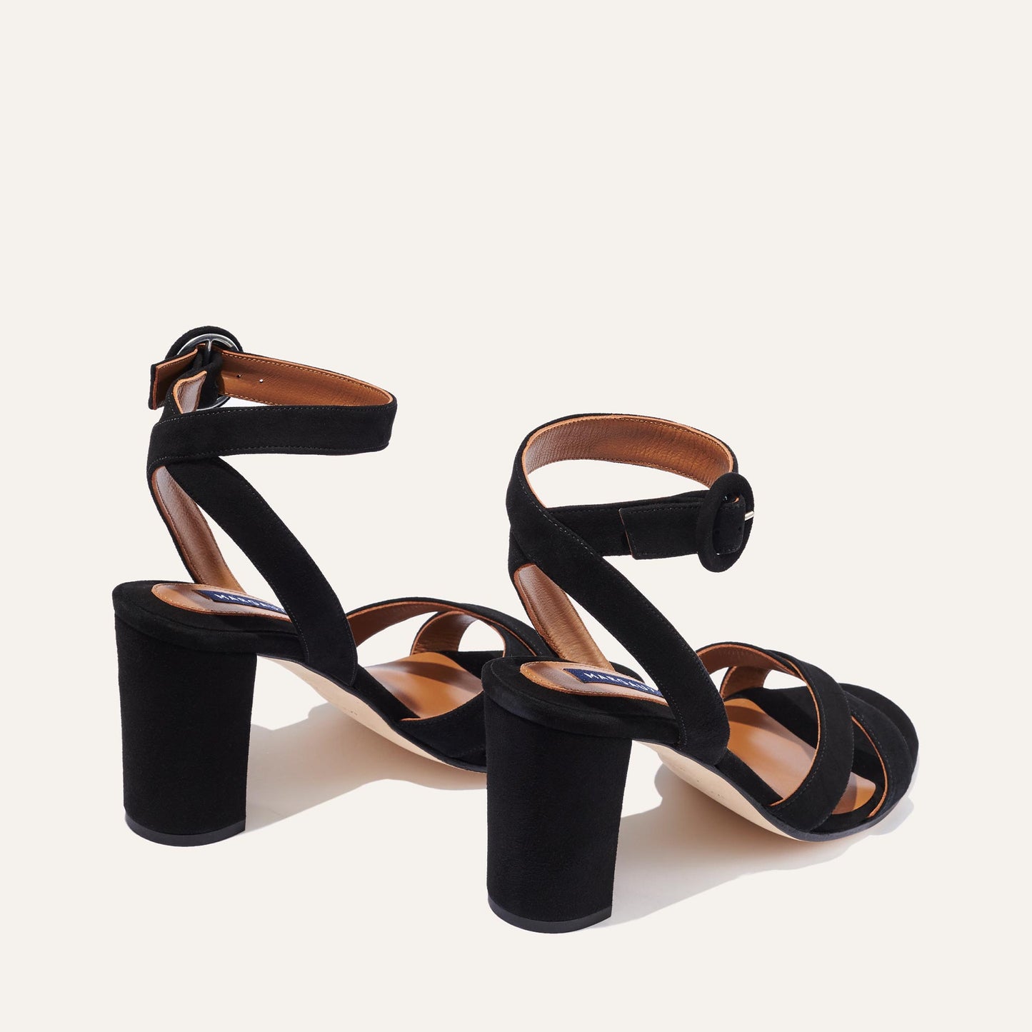 The Uptown Sandal - Black Suede by margaux-development features thick block heels, crisscross front straps, and ankle straps with round buckles for all-day comfort, shown against a plain light background.