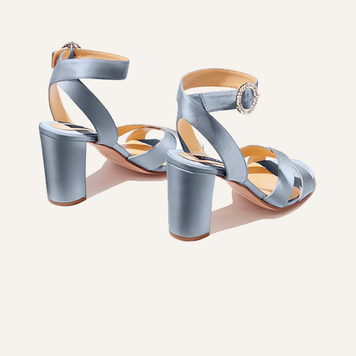 The Uptown Sandal - Powder Satin with Crystal Buckle by margaux-development is a light blue satin high-heeled sandal with block heels, crisscross straps, and a rhinestone ankle buckle, designed for all-day comfort against a plain background.