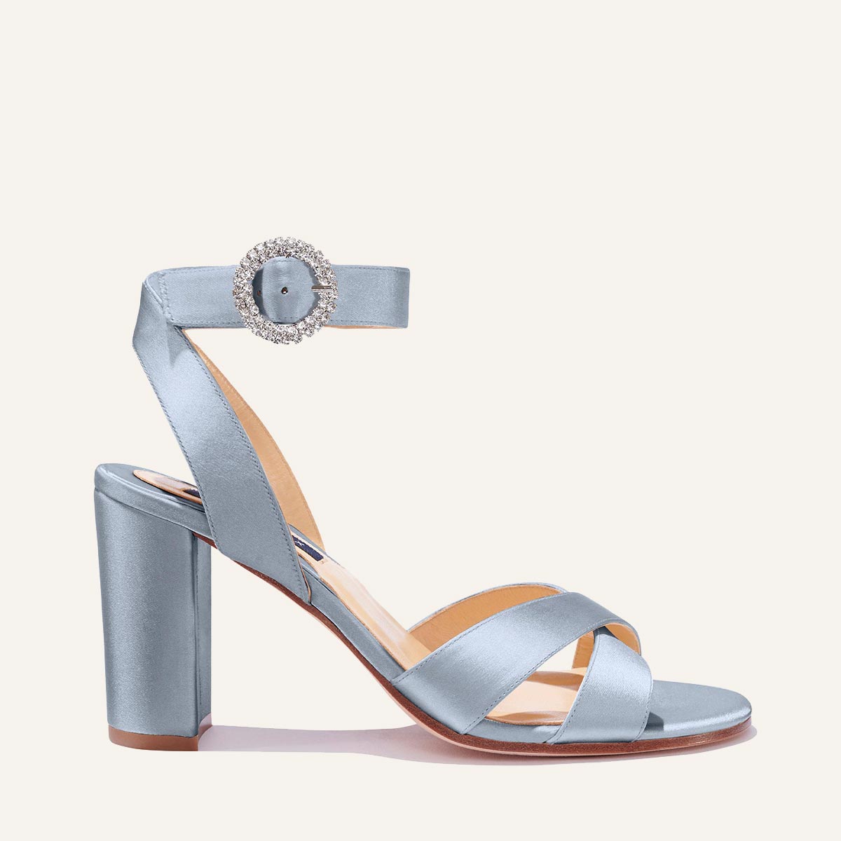 The Uptown Sandal - Powder Satin with Crystal Buckle by margaux-development features a block heel, crisscross toe straps, ankle strap, and crystal buckle, plus a cushioned tan insole and sturdy sole for all-day comfort.