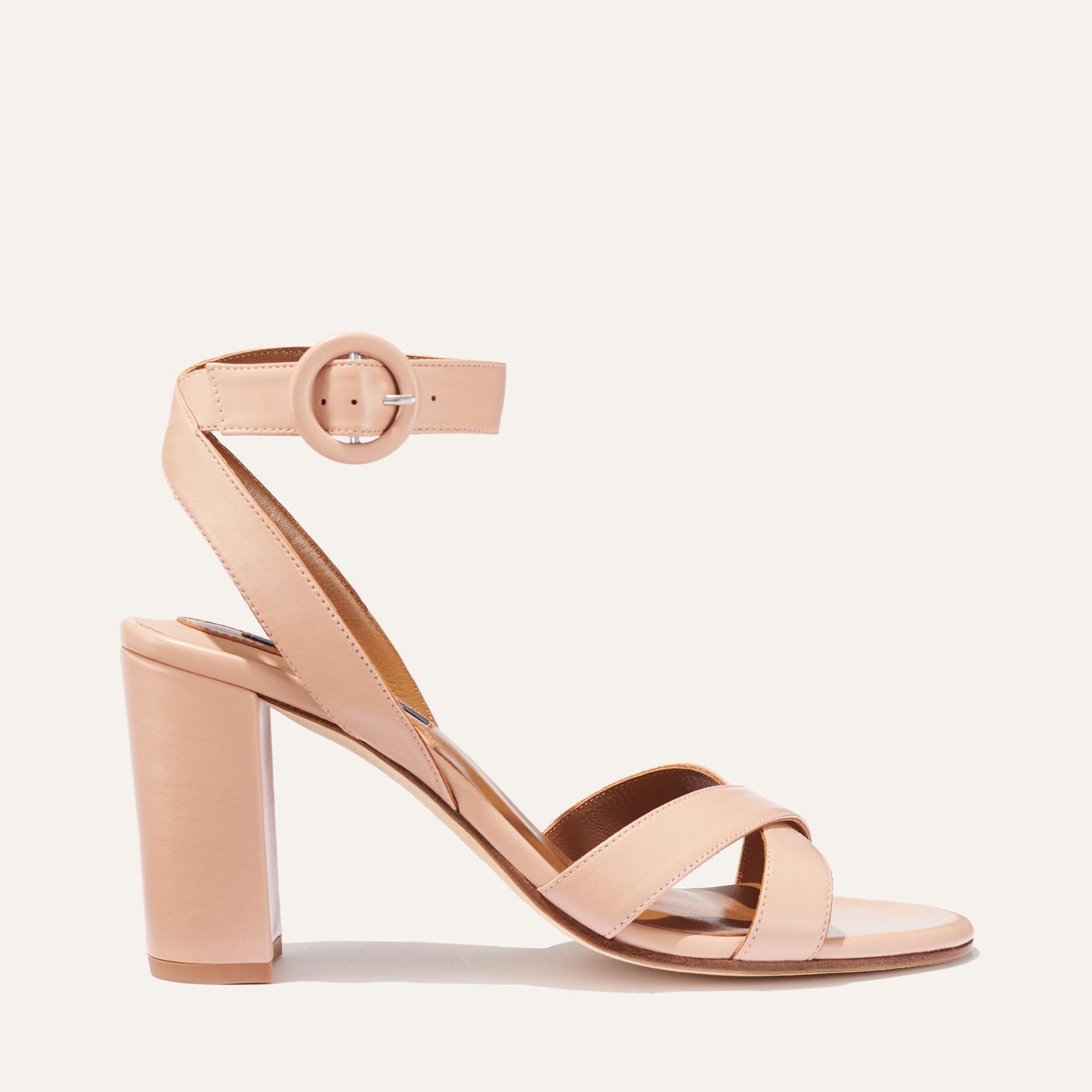 The Uptown Sandal - Rose Nappa by margaux-development features a nude hue, thick block heel, two slim crossing toe straps, and an ankle strap with a round buckle—styled in side profile against a plain background for all-day comfort.